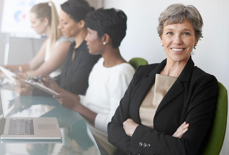 older business woman sitting at a table with colleagues smiling at the camera older business woman sitting at a table with colleagues smiling at the camera